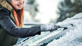 A woman scraping ice off a car windshield
