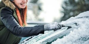 A woman scraping ice off a car windshield