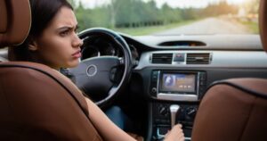 A confused looking young woman turning her head to look towards the rear of her vehicle as she sits in the driver seat