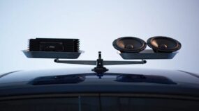 A balanced scale on top of a car with an amplifier on one side of the scale and two speakers on the other