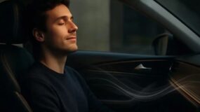 A man sitting inside a car whith his eyes closed listening to music with a smile on his face