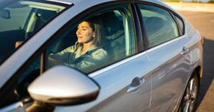 A woman driving a gray car with the sun on her face